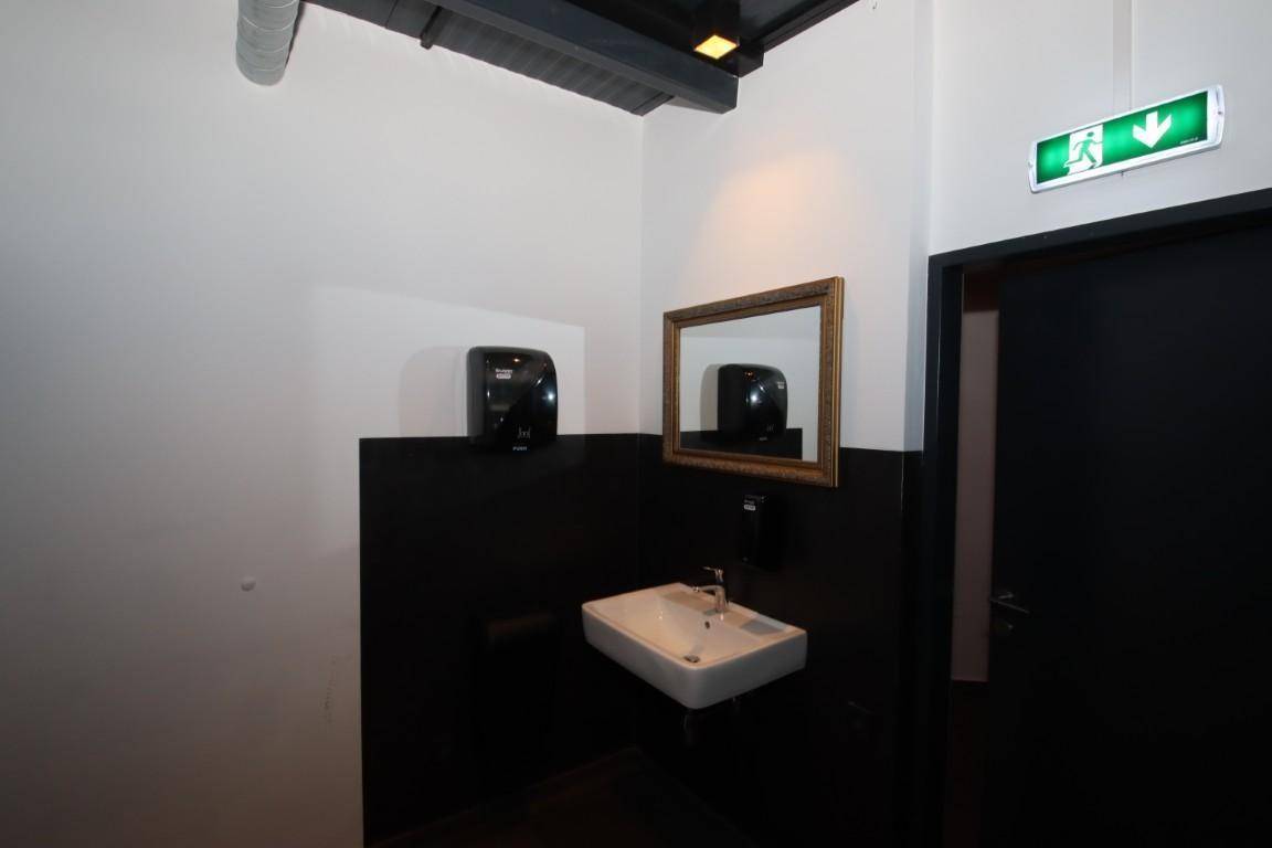 Waschbereich mit modernem Waschbecken, Spiegel und Seifenspender in dunkler Umgebung.