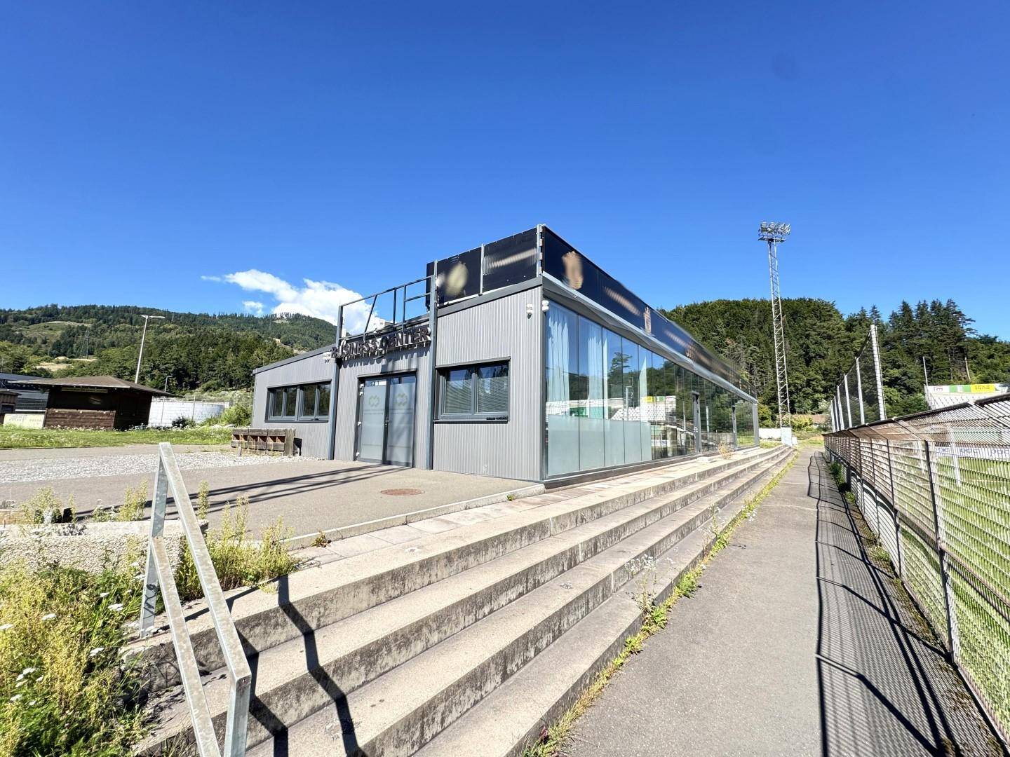 Ansicht des modernen Gebäudes mit großer Glasfront und Treppenaufgang zum Sportfeld.