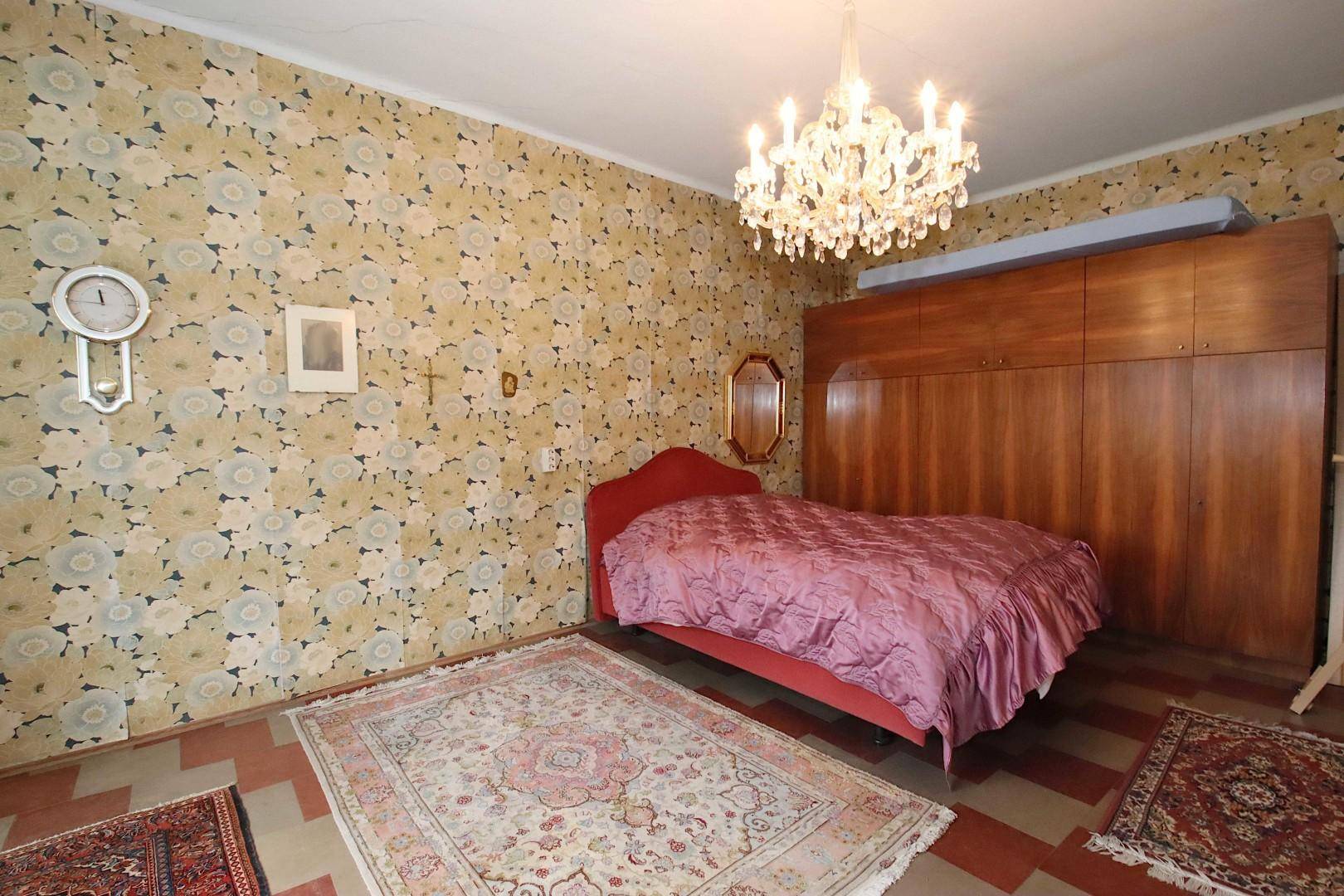 Schlafzimmer mit auffälliger floraler Tapete, großem Holzschrank und Doppelbett.
