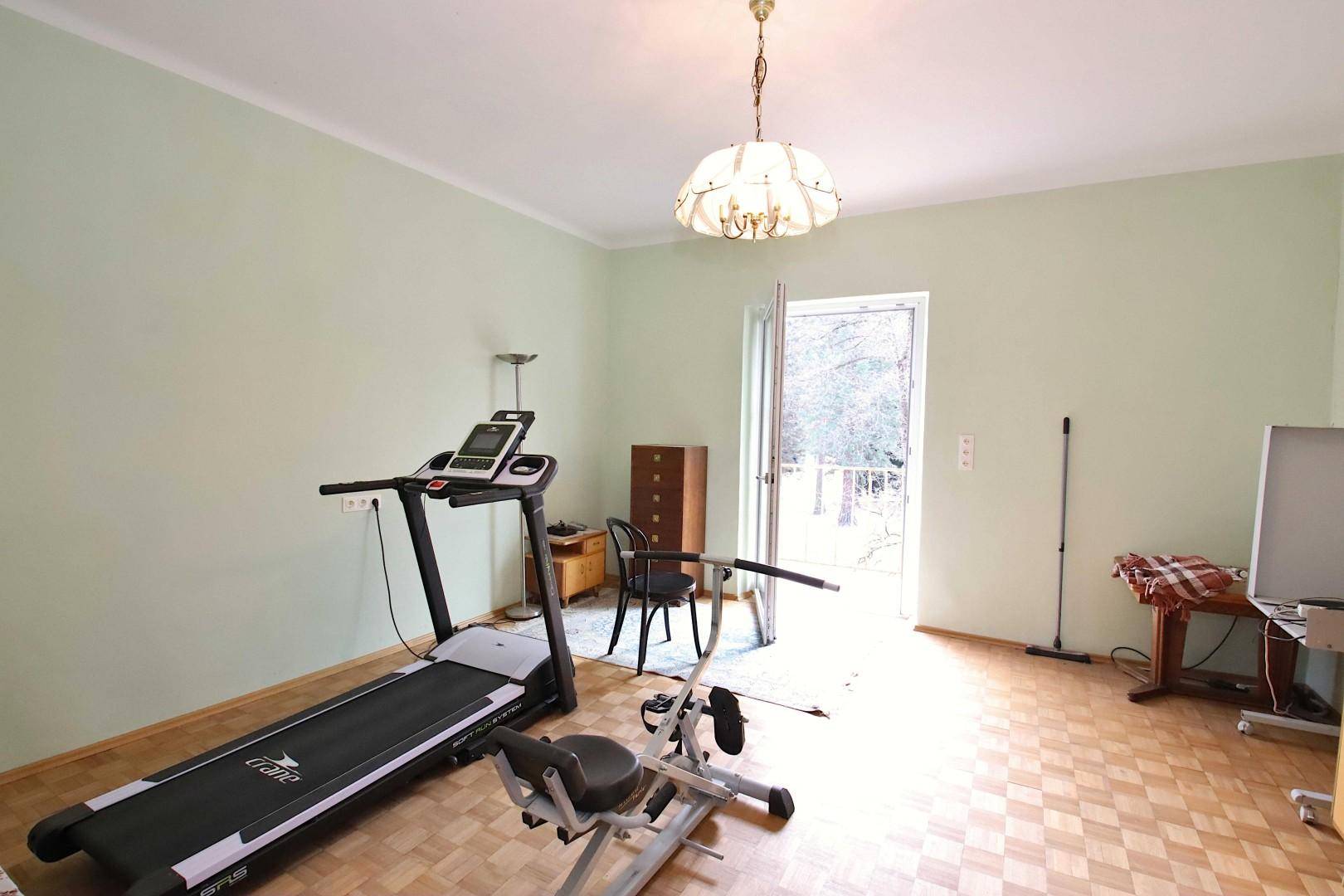 Raum mit Fitnessgeräten, Parkettboden und Zugang zu einem Außenbereich.