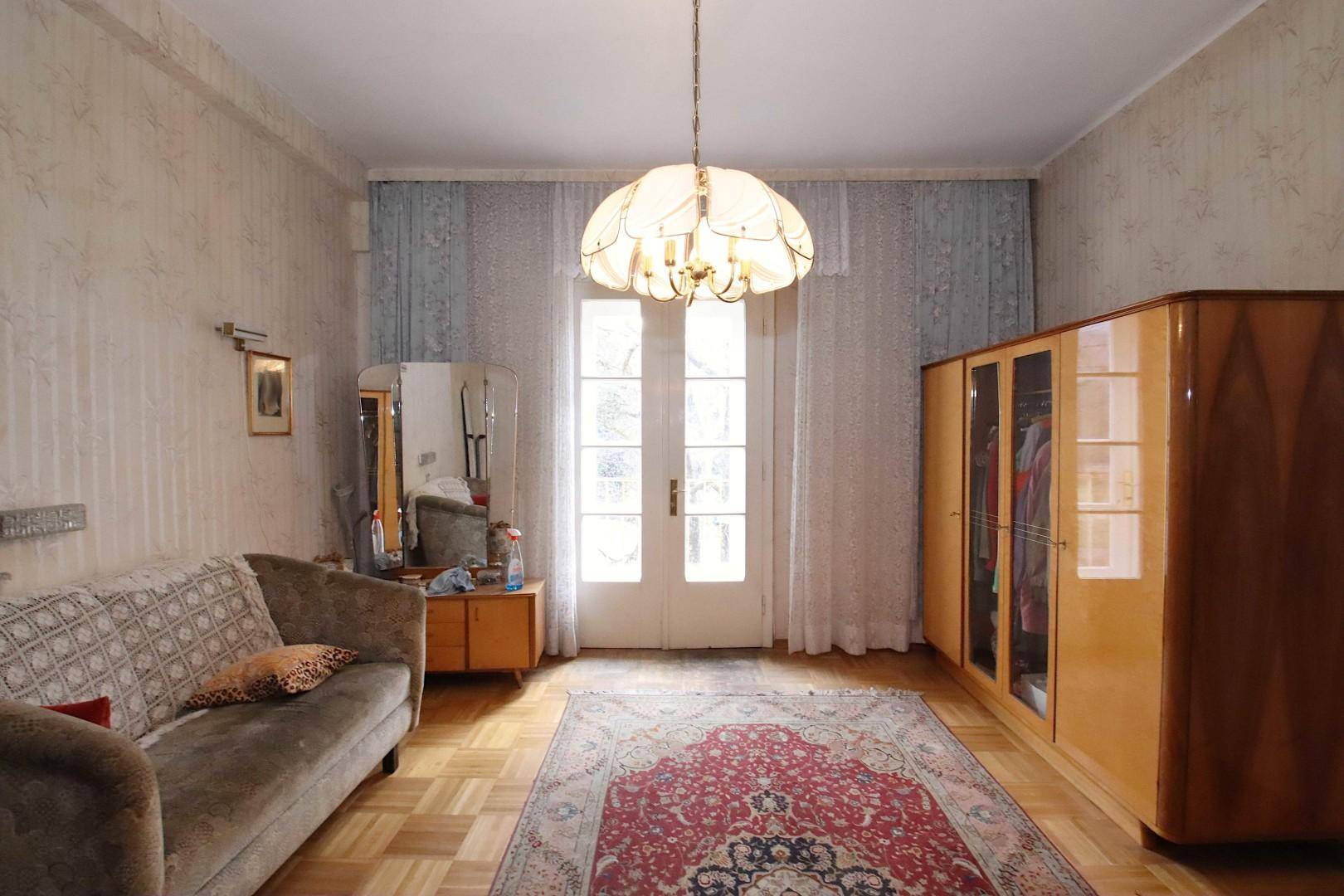 Schlafzimmer mit Parkettboden, Vintage-Sofa, Holzschrank und Zugang zu einem französischen Balkon.