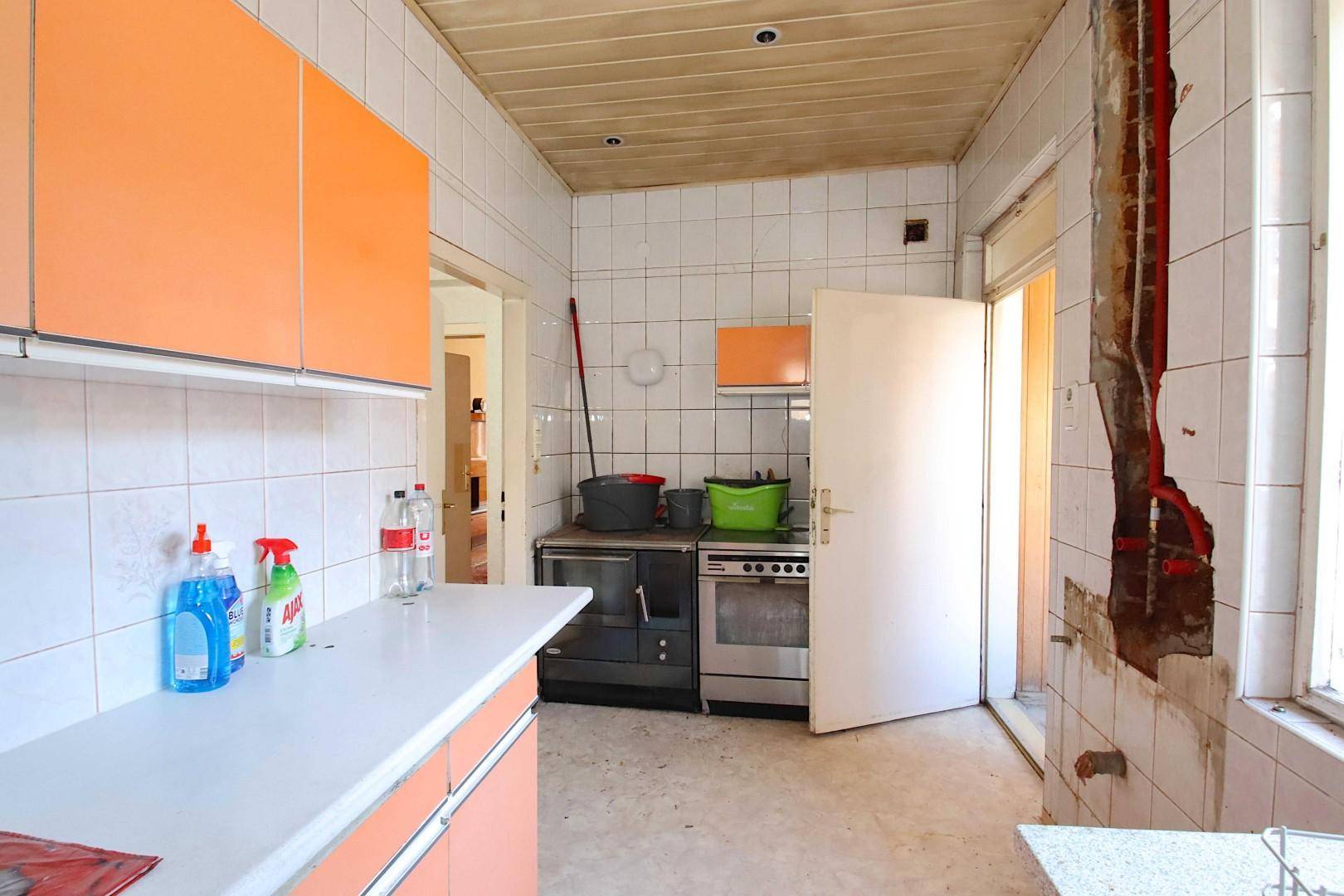 Küche in Renovierung mit orangefarbenen Schränken, Fliesen und freigelegten Wänden.