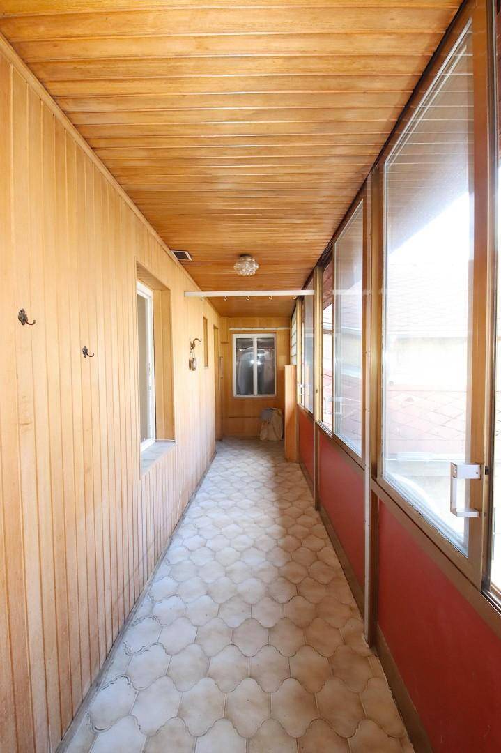 Heller, verglaster Gang mit Holzverkleidung und Fliesenboden.