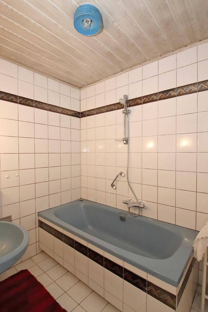 Badezimmer mit blauer Badewanne, weißen Fliesen und Holzdecke.