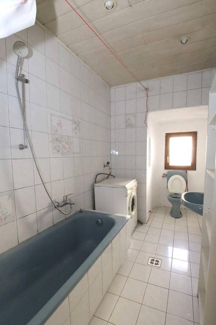 Badezimmer mit blauer Badewanne, WC, Waschmaschine und Fliesenboden.