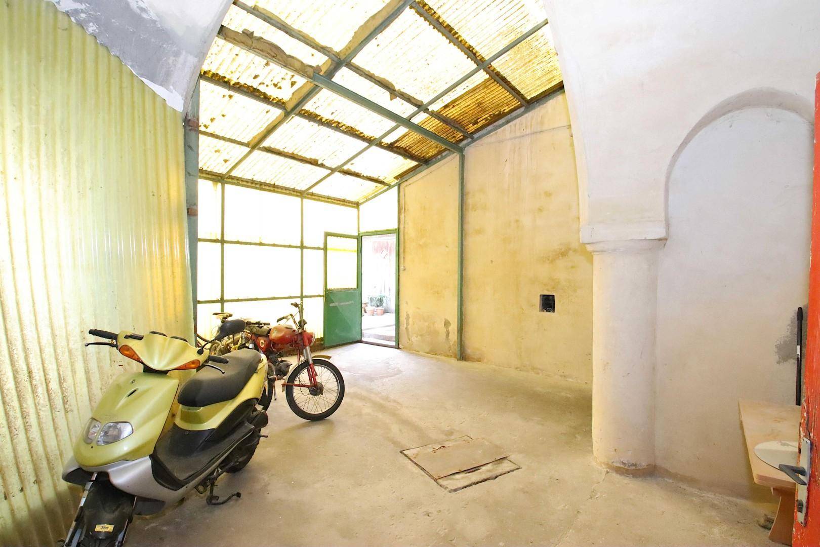 Große Garage mit Wellblechdach, Motorrollern und Betonboden.