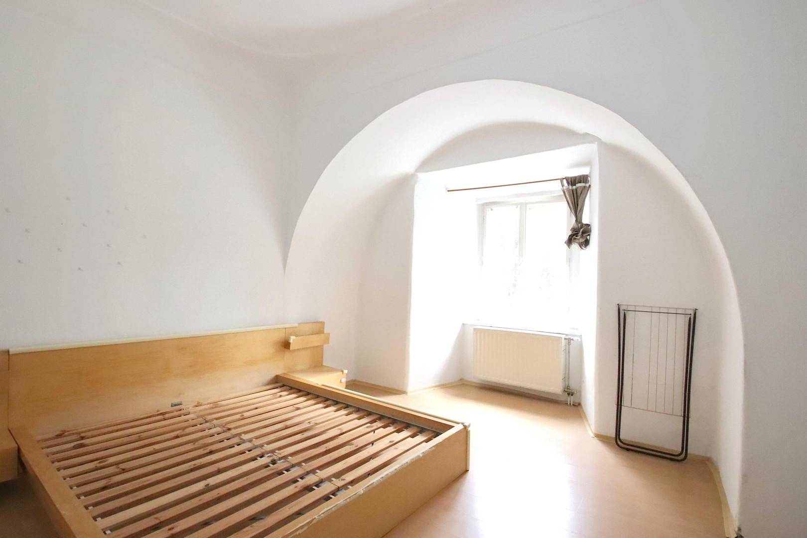 Schlafzimmer mit Gewölbedecke, Parkettboden und einem Fenster in einer Nische.
