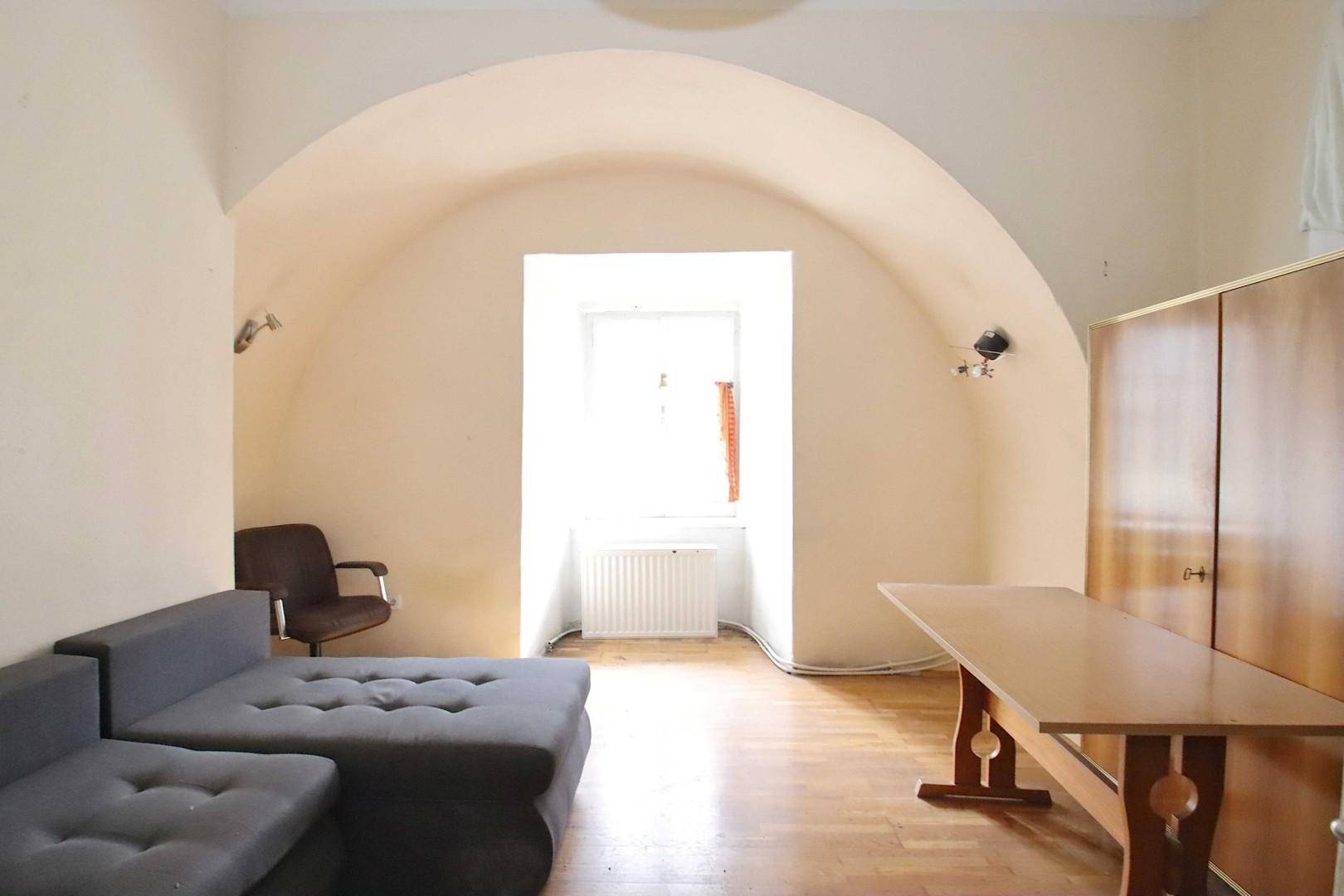 Wohnzimmer mit Gewölbedecke, Parkettboden und einem Sofa in der Fensternische.