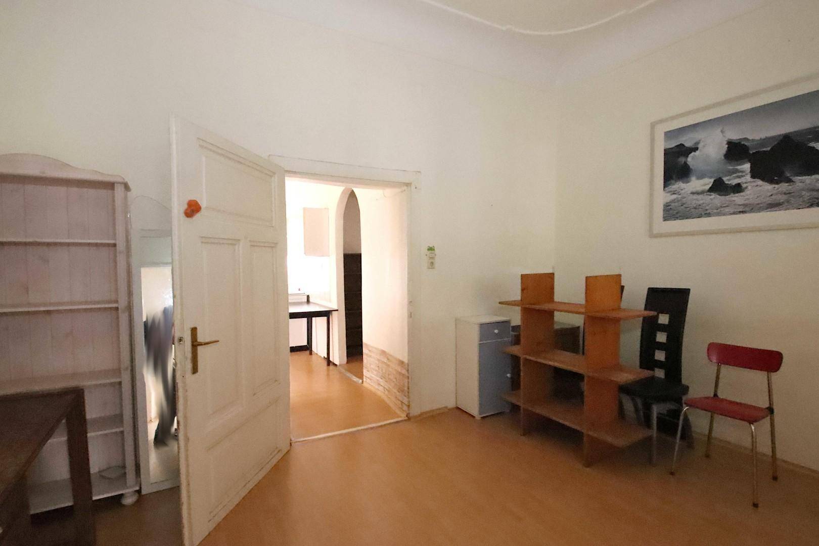 Heller Raum mit Parkettboden, Regalen und offenem Durchgang zu einem weiteren Zimmer.