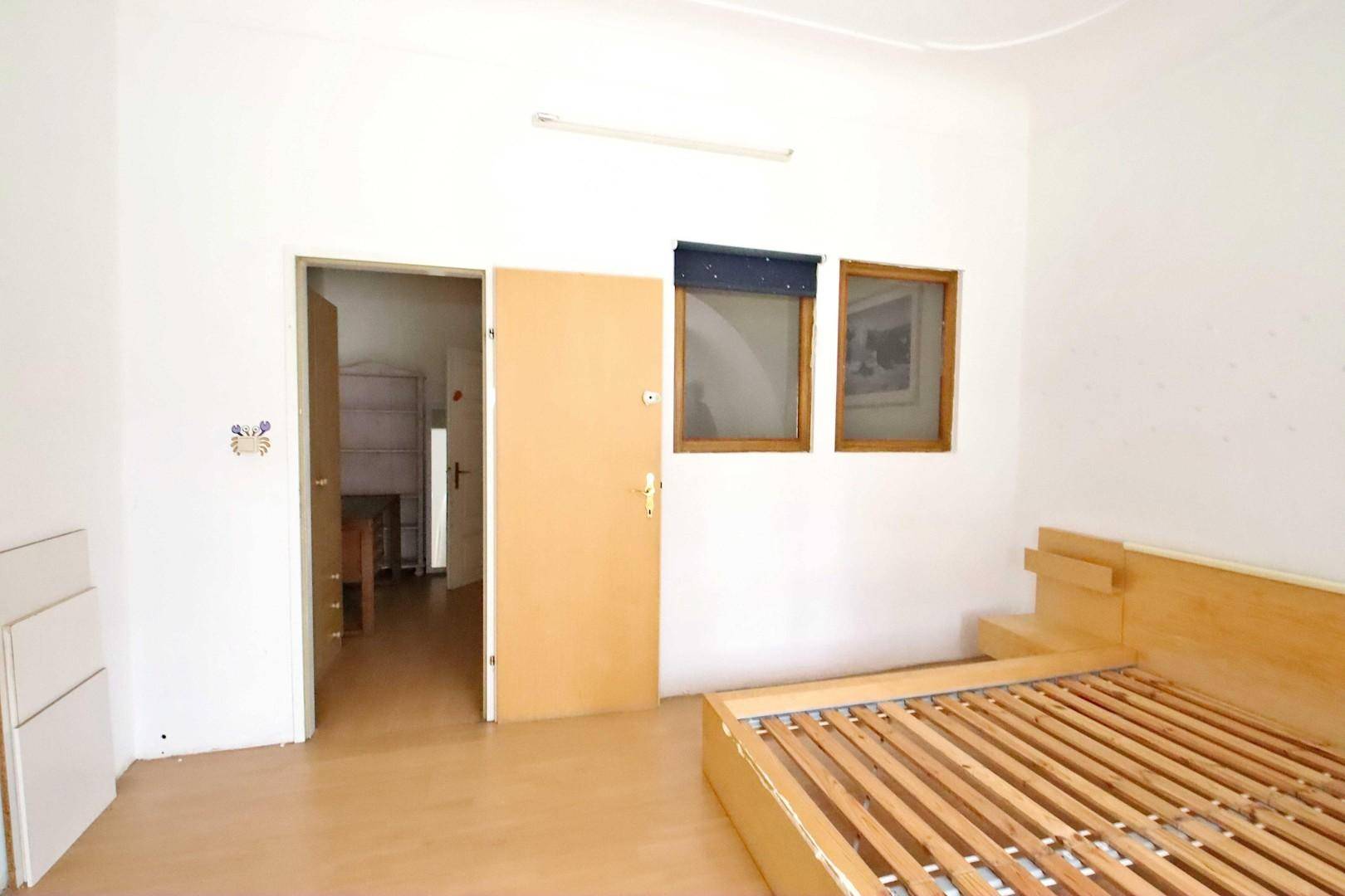 Schlafzimmer mit hellem Holzbettrahmen, Parkettboden und Fenster.