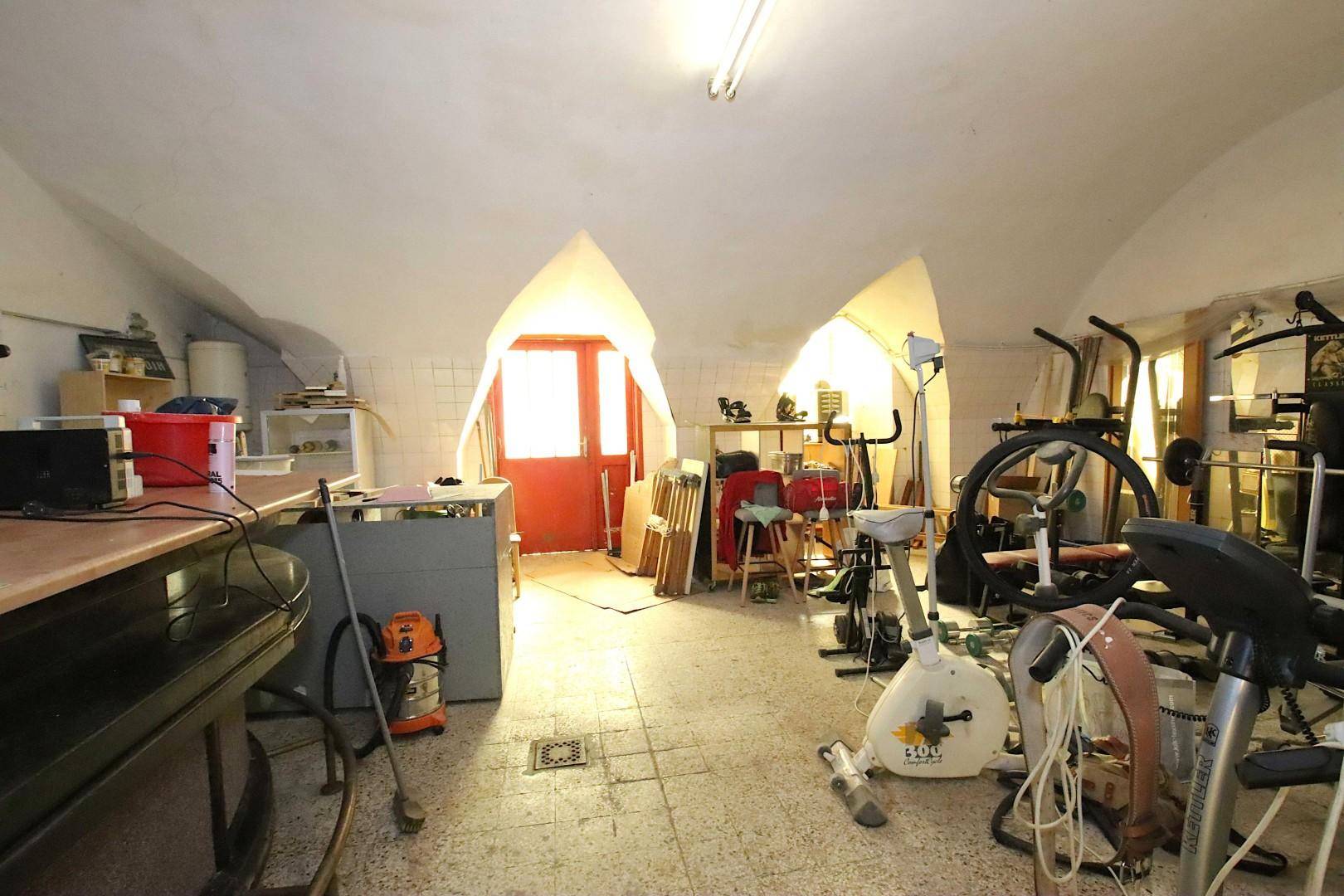 Kellerraum mit Fitnessgeräten, Fliesenboden und gewölbter Decke.