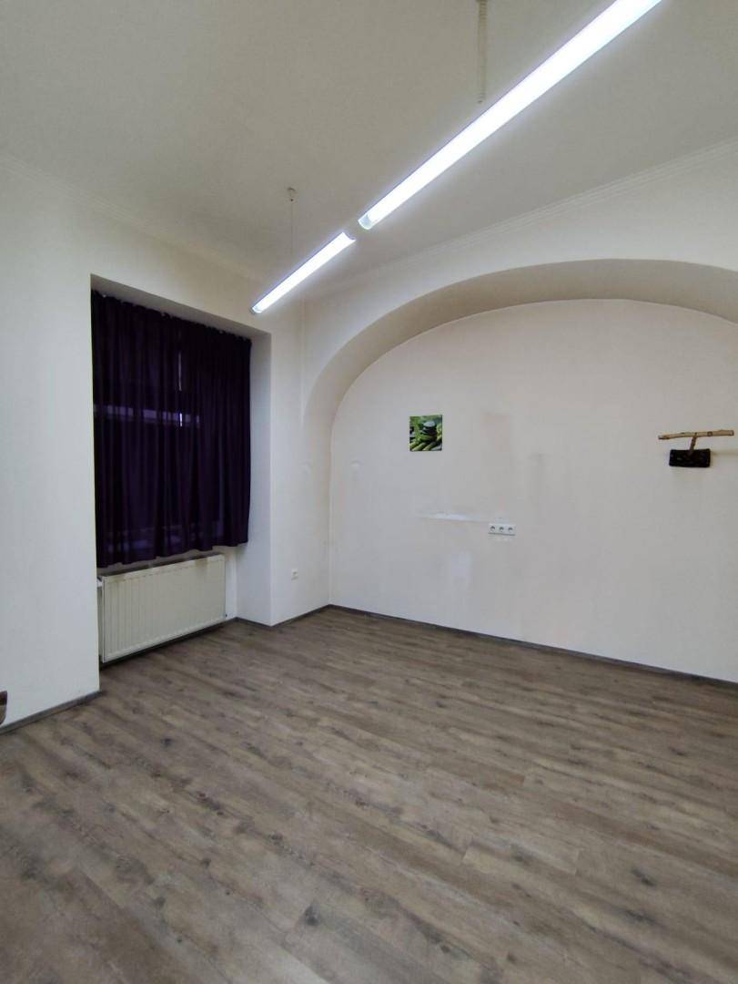 Leerer Raum mit Holzlaminatboden, einem Fenster mit dunklen Vorhängen und einer gewölbten Wandstruktur.