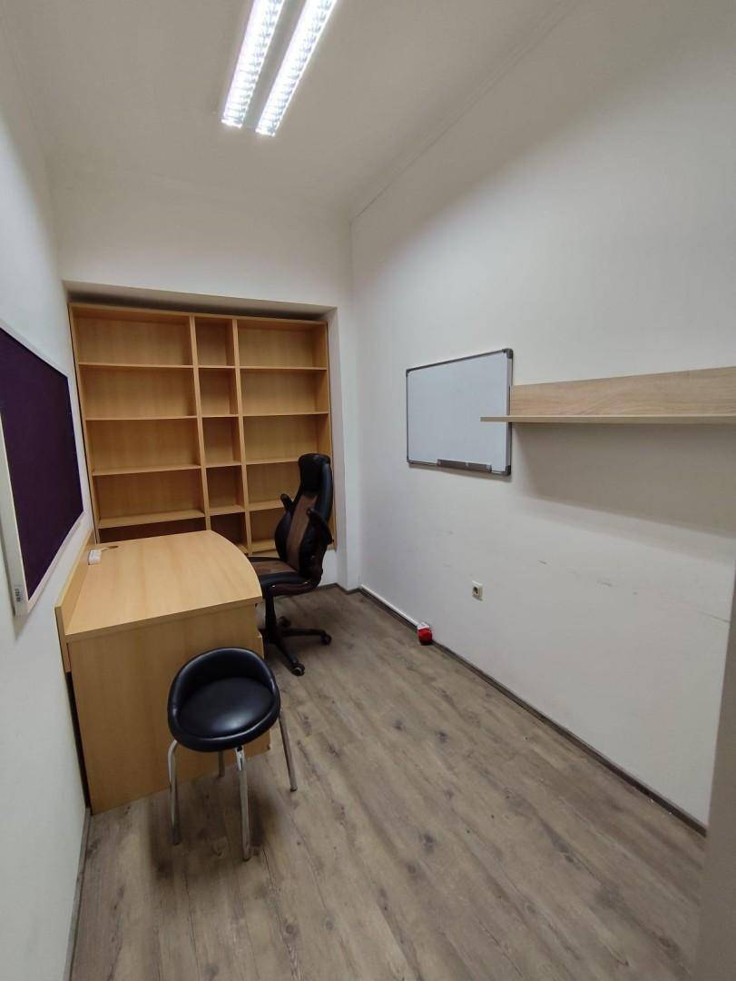 Funktionales Büro mit Holzlaminatboden, einem Schreibtisch, Bürostuhl und leeren Holzregalen.