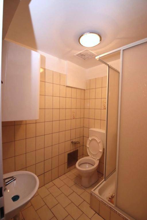 Badezimmer mit beigefarbenen Fliesen, Toilette, Waschbecken und einer einfachen Duschkabine.