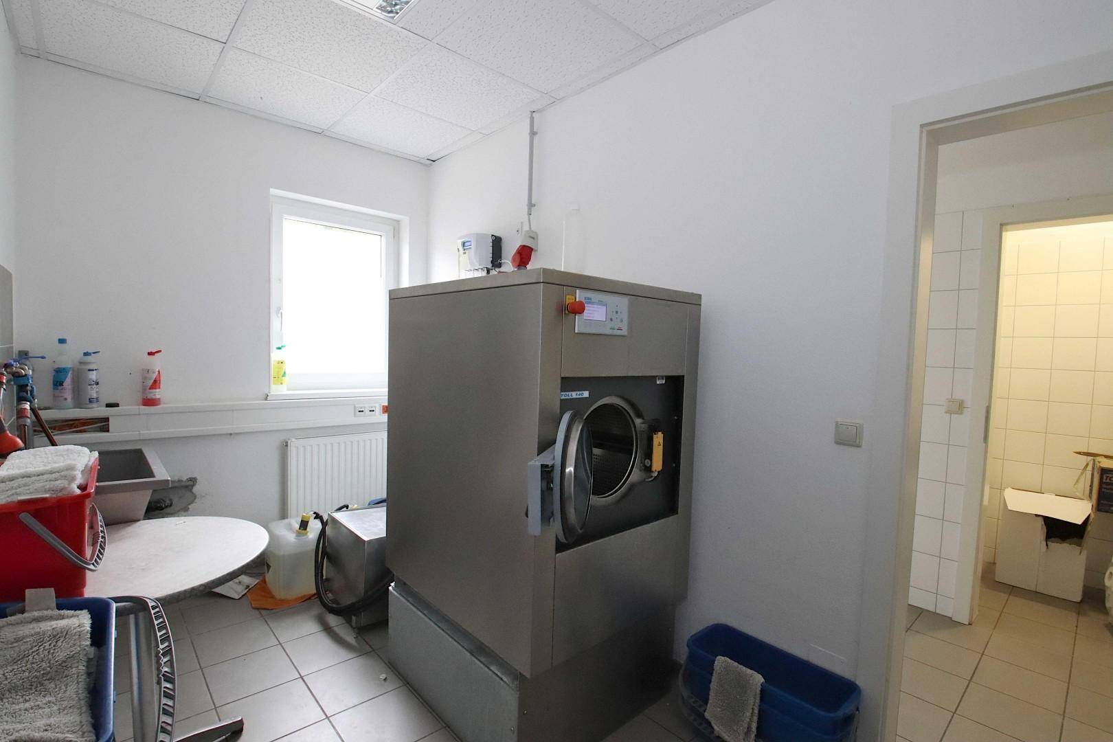 Waschküche mit Industriegerät, Fenster und gefliestem Boden, bereit für den Betrieb.