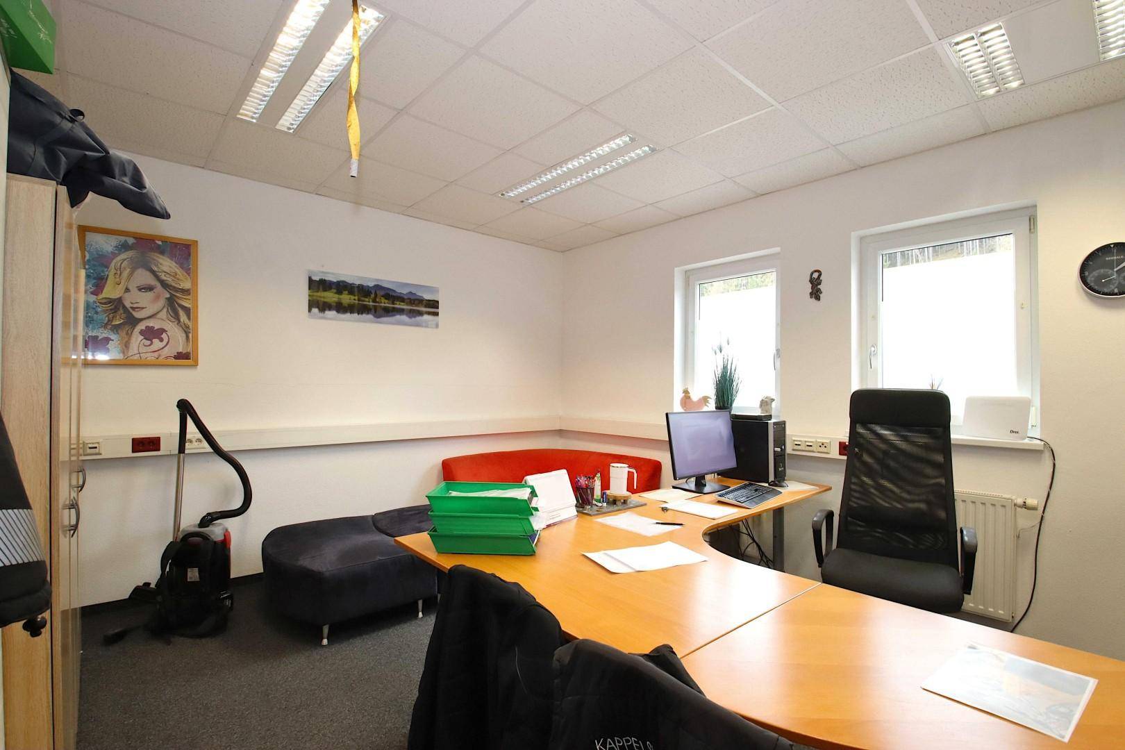 Helles Büro mit Teppichboden, zwei Fenstern und einem großen Schreibtischbereich.