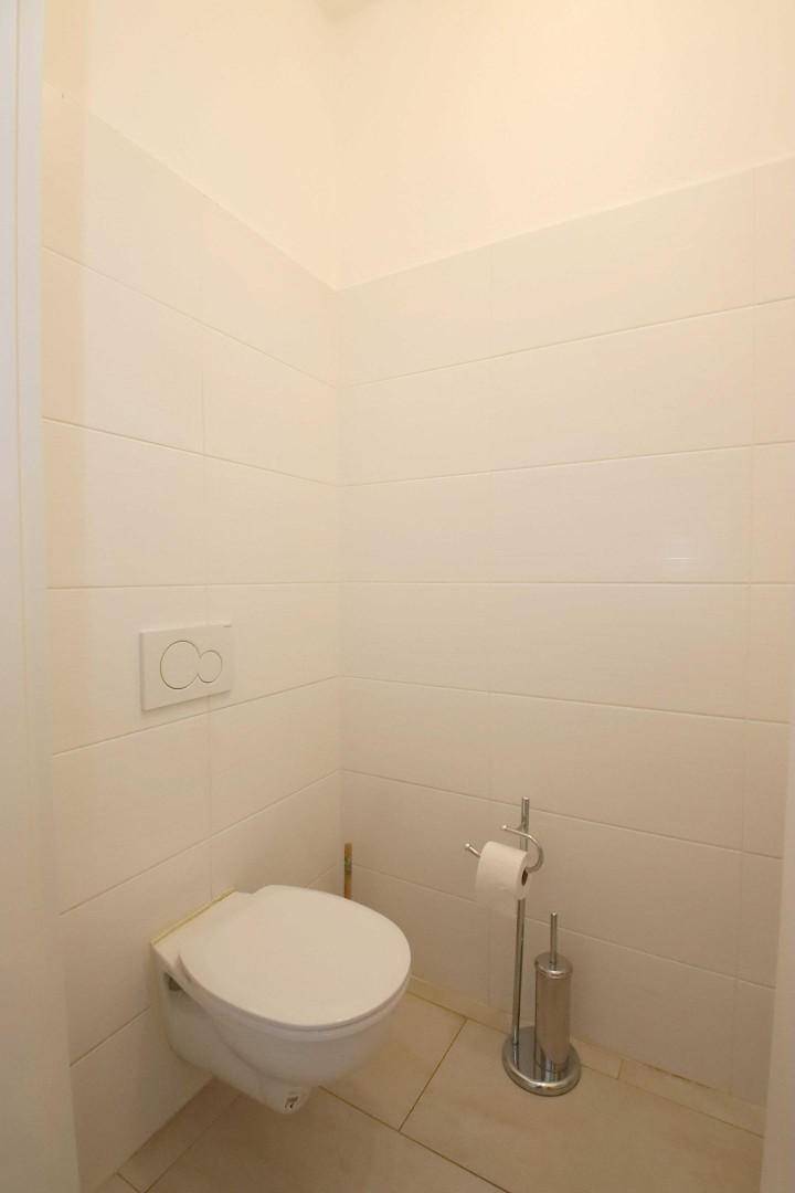 Separates WC mit wandhängender Toilette und hellen Fliesen an Wänden und Boden.