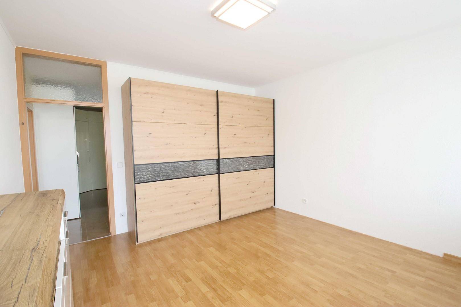 Schlafzimmer mit großem Holzschrank und hellem Laminatboden, bereit zur individuellen Einrichtung.