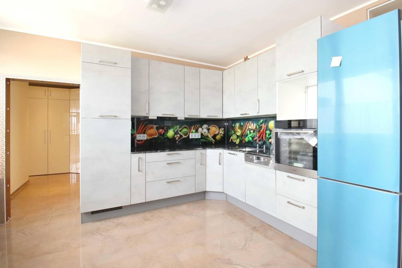Moderne Küche mit weißen Schränken, blauem Kühlschrank und farbenfroher Rückwand.