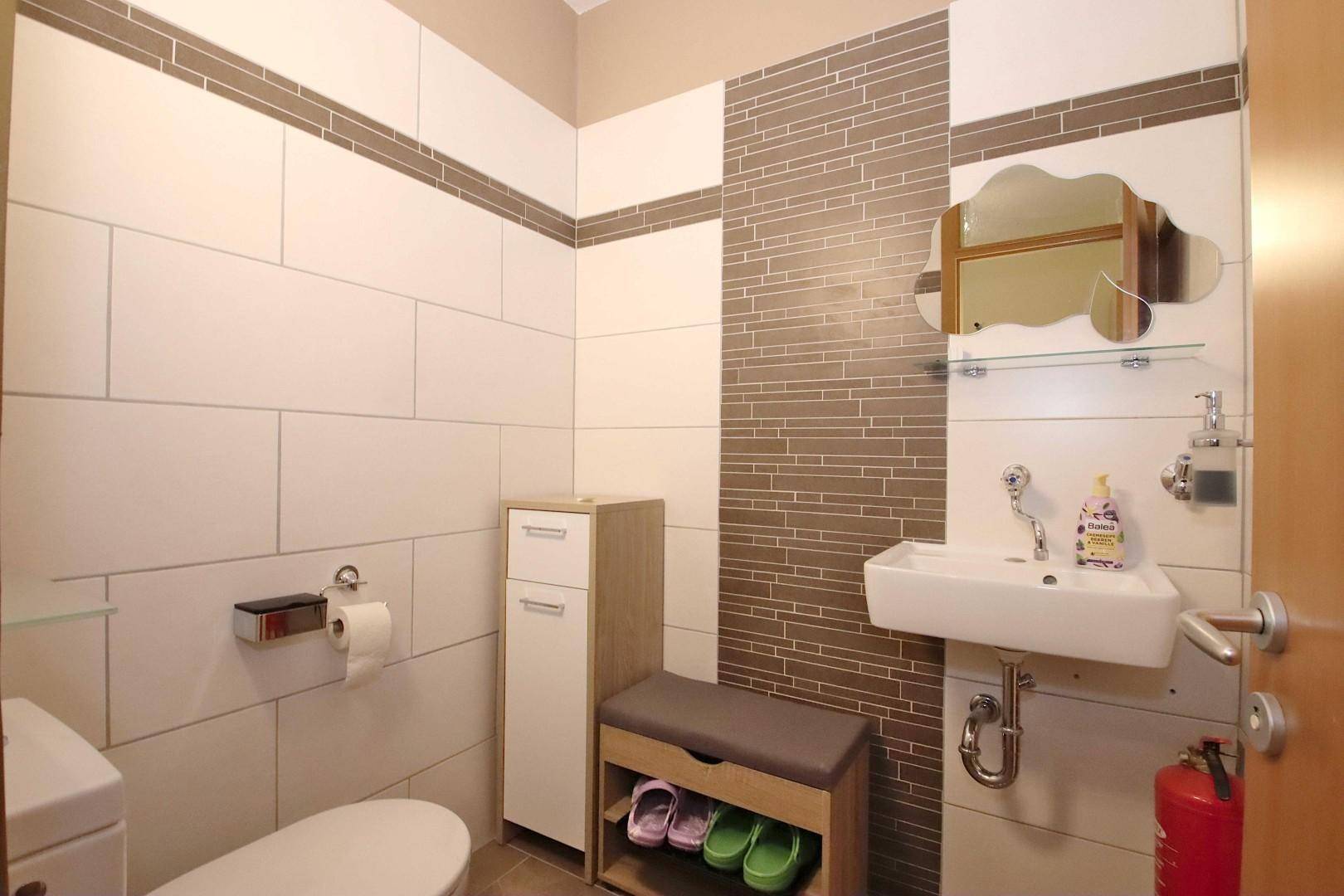 Modern gefliestes Gäste-WC mit Waschbecken und Spiegel, in hellen und braunen Farbtönen.