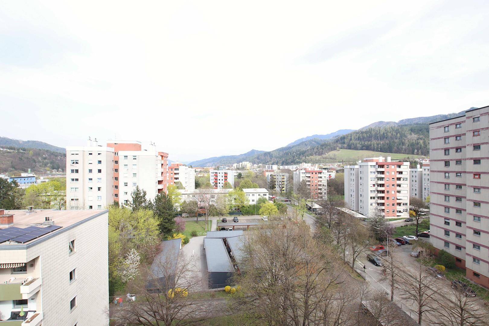 Weitläufiger Blick über eine städtische Wohngegend mit vielen Gebäuden und Bergen im Hintergrund.