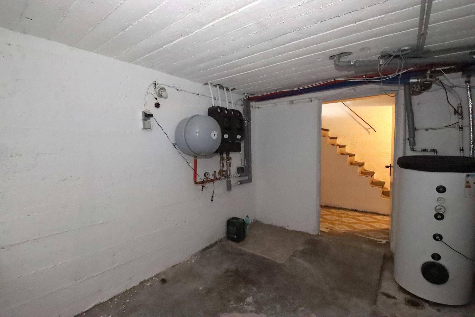 Kellerraum mit Heizungsinstallationen und Zugang zu weiteren Bereichen.