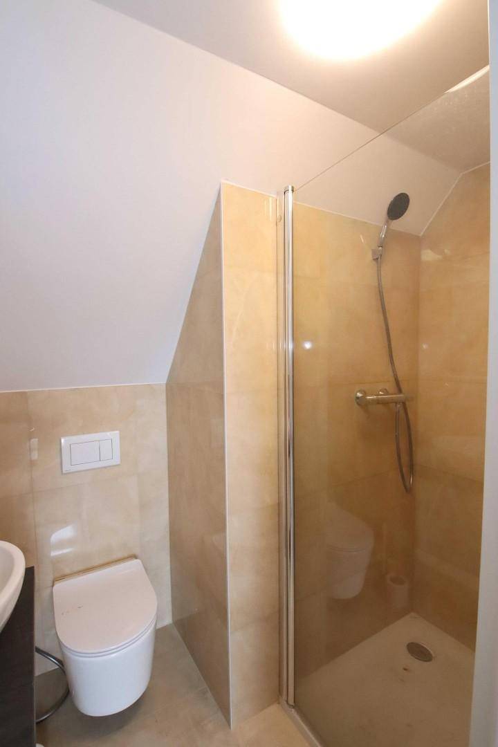 Modernes Badezimmer im Dachgeschoss mit Dusche, WC und beigefarbenen Fliesen.