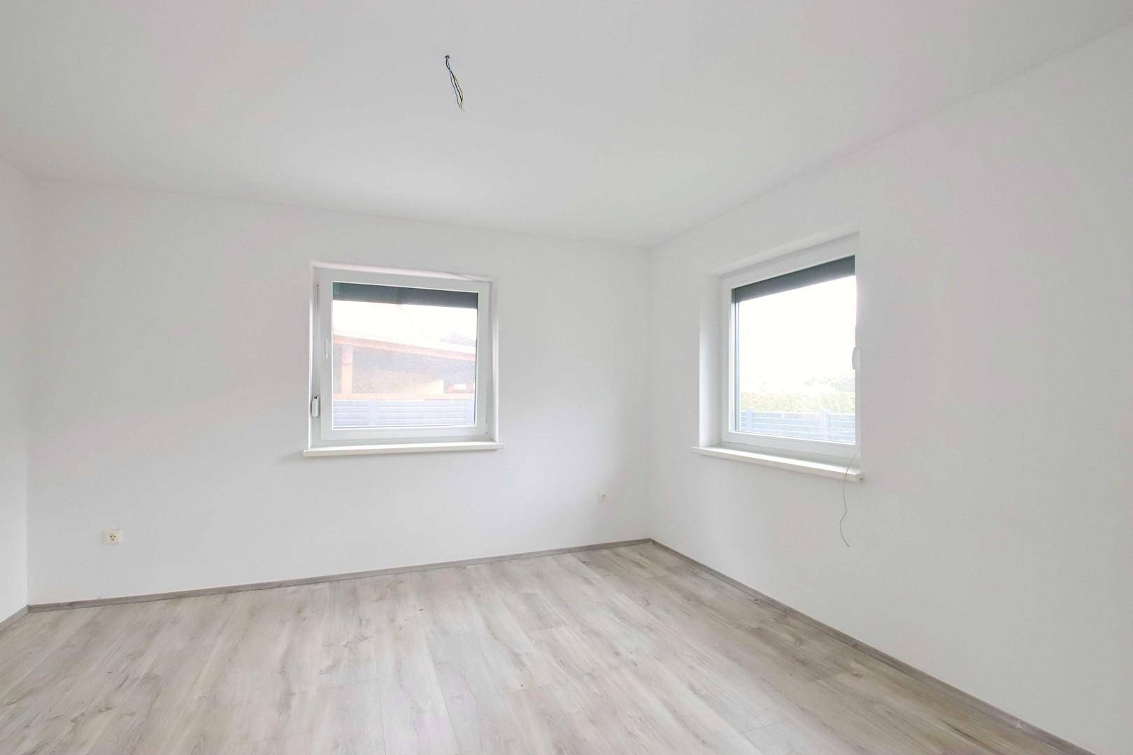 Geräumiges Schlafzimmer mit zwei Fenstern und hellem Laminatboden.