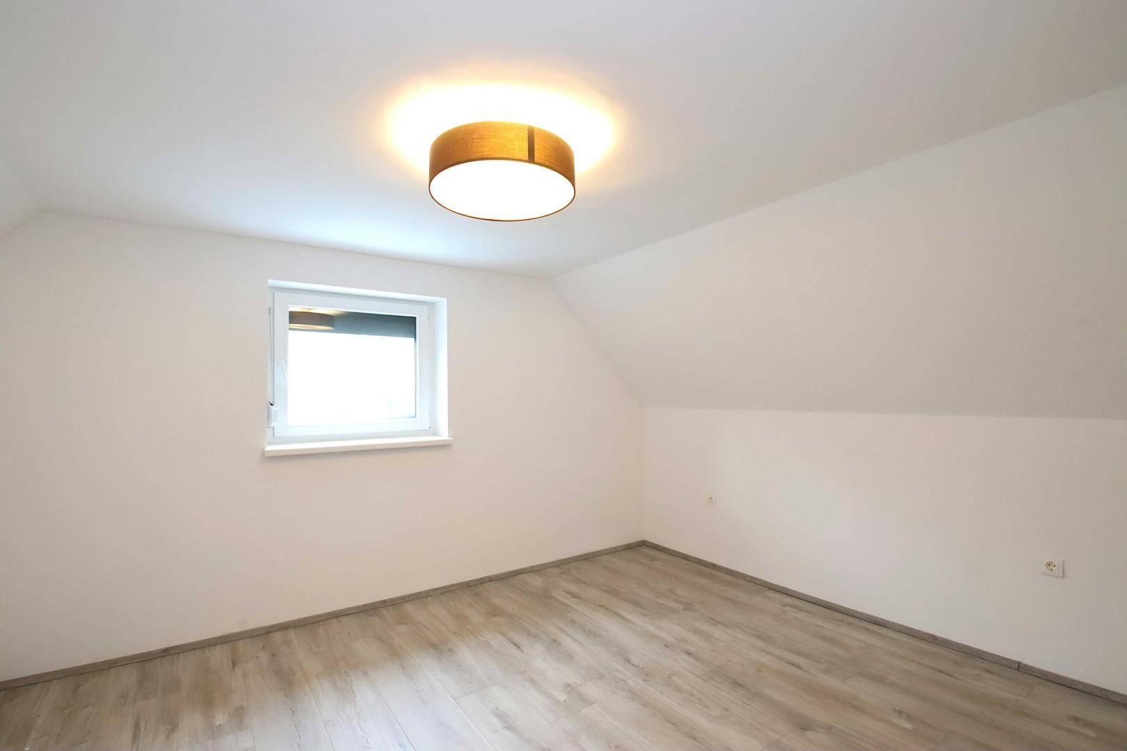 Helles Schlafzimmer im Dachgeschoss mit schräger Decke und Laminatboden.
