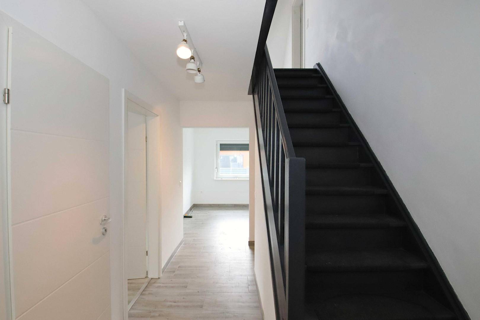 Heller Flur mit dunkler Holztreppe und modernem Laminatboden.