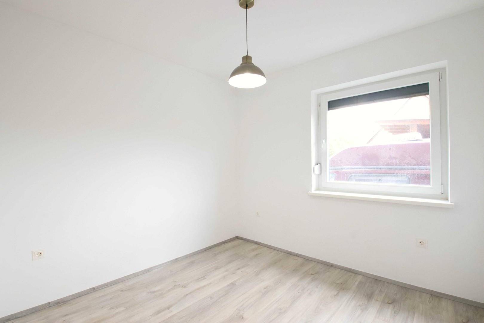 Helles Schlafzimmer mit Laminatboden und einem Fenster, das viel Licht hereinlässt.