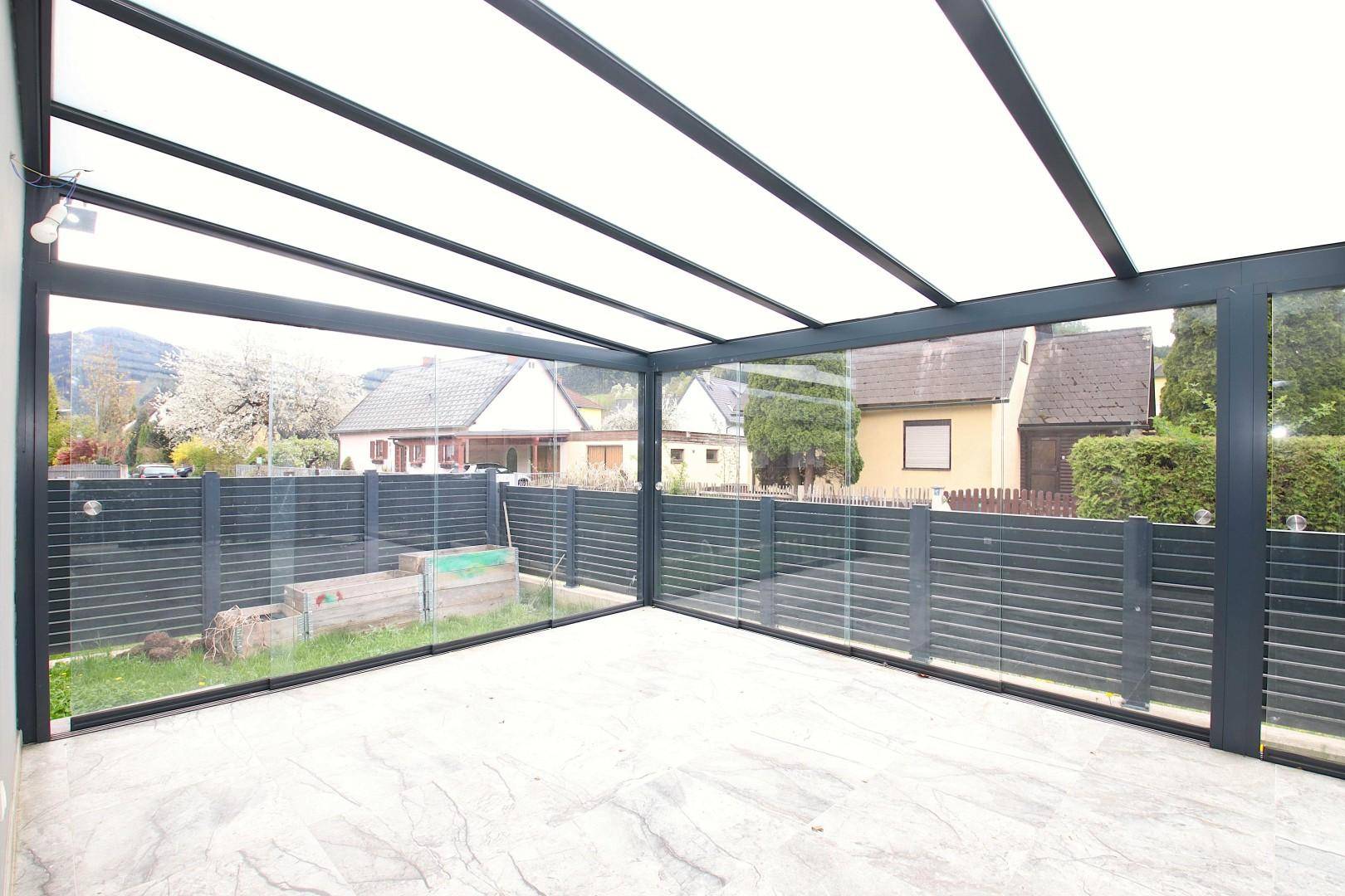 Heller Wintergarten mit Glaswänden und Fliesenboden, bietet einen Blick ins Grüne.