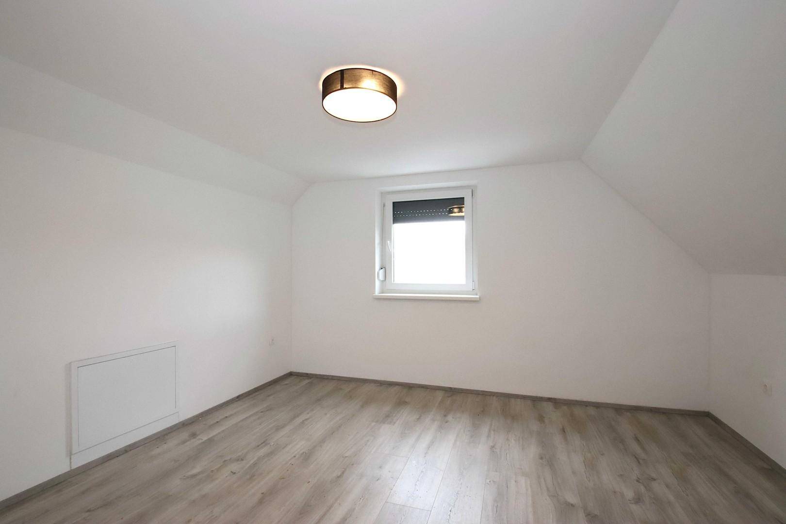 Dachgeschosszimmer mit Laminatboden und einem Fenster, das für natürliche Belichtung sorgt.