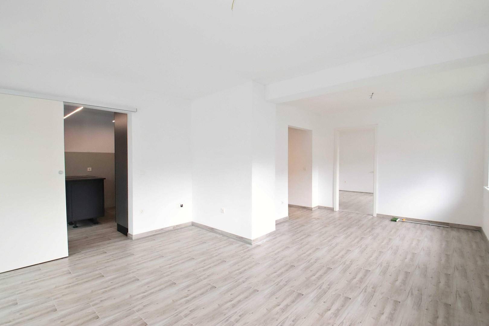 Offener Wohnbereich mit hellem Laminatboden und mehreren Türöffnungen.