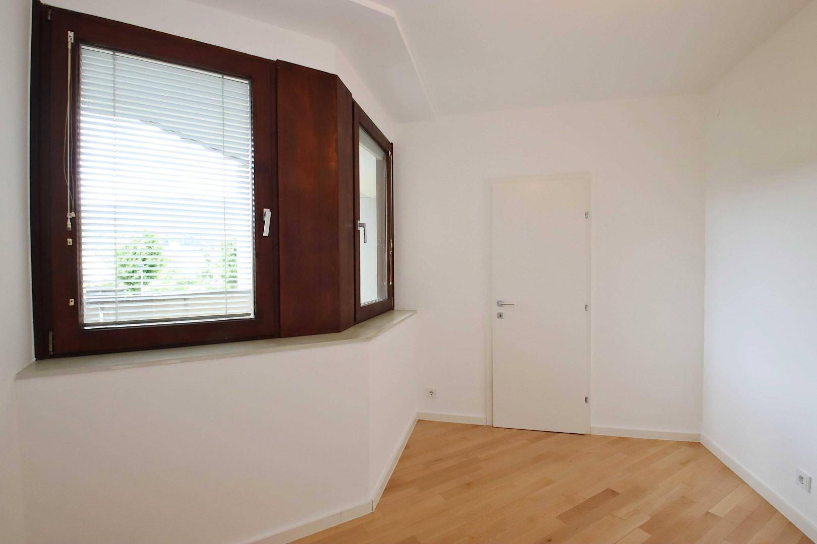 Helles, leeres Zimmer mit Holzboden und großen Fenstern, bereit zur individuellen Gestaltung.