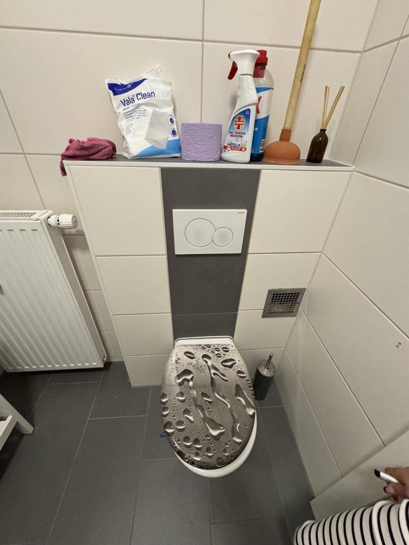 Modernes WC mit wandhängender Toilette, grauen Bodenfliesen und weißer Wandverkleidung.