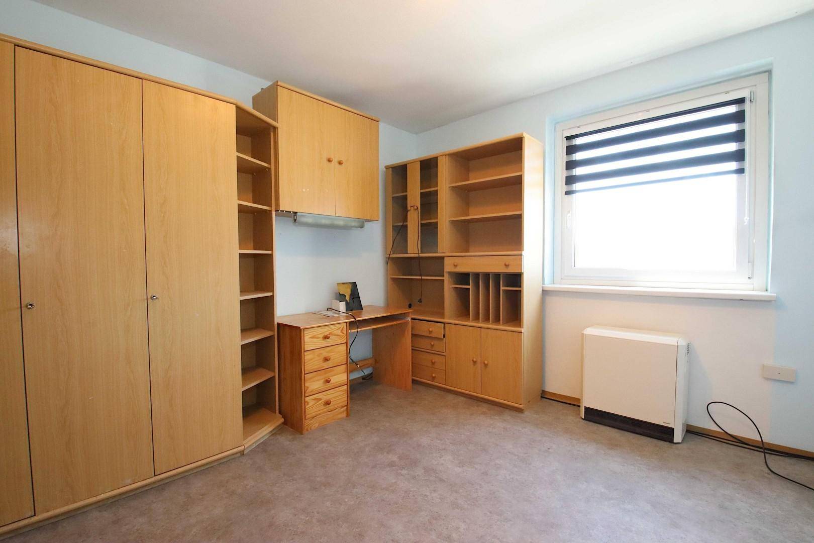 Schlafzimmer oder Arbeitszimmer mit Holzmöbeln, Teppichboden und großem Fenster.