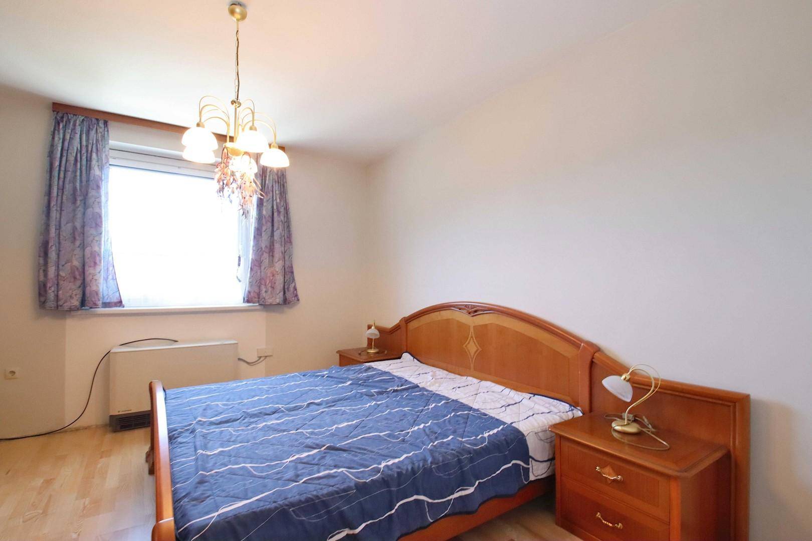 Helles Schlafzimmer mit Doppelbett, Nachttischen und einem Fenster mit Vorhängen.