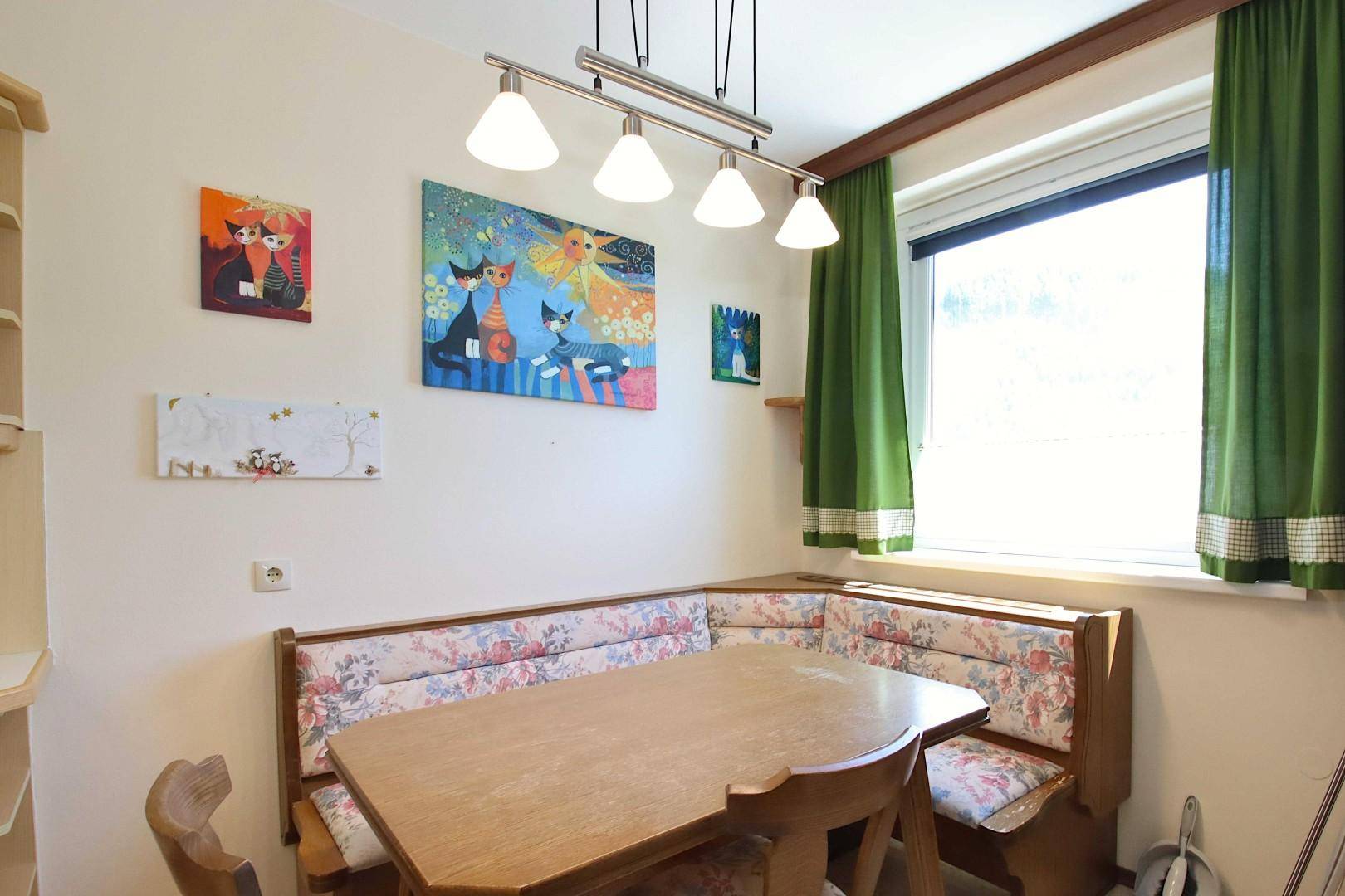 Gemütliche Essecke in der Küche mit Eckbank, Holztisch und bunten Bildern an der Wand.