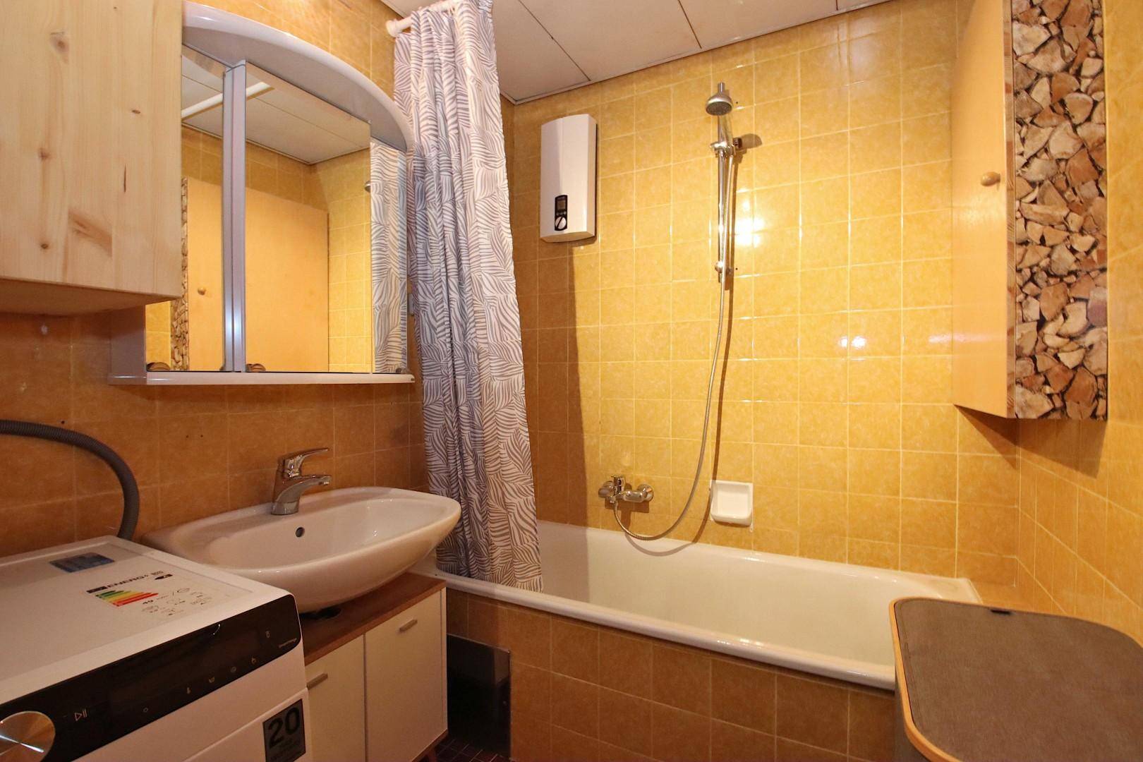 Badezimmer mit gelben Fliesen, Badewanne mit Duschfunktion und Waschmaschine.