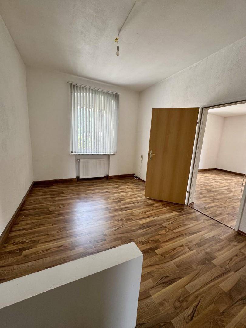 Leerer Raum mit Laminatboden und Fenster mit Jalousien, bereit zur individuellen Gestaltung.
