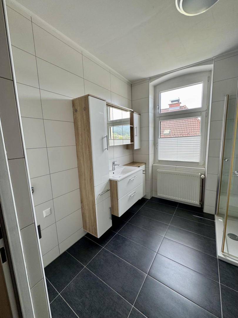 Modernes Badezimmer mit dunklen Bodenfliesen, weißer Wandverkleidung und Fenster.