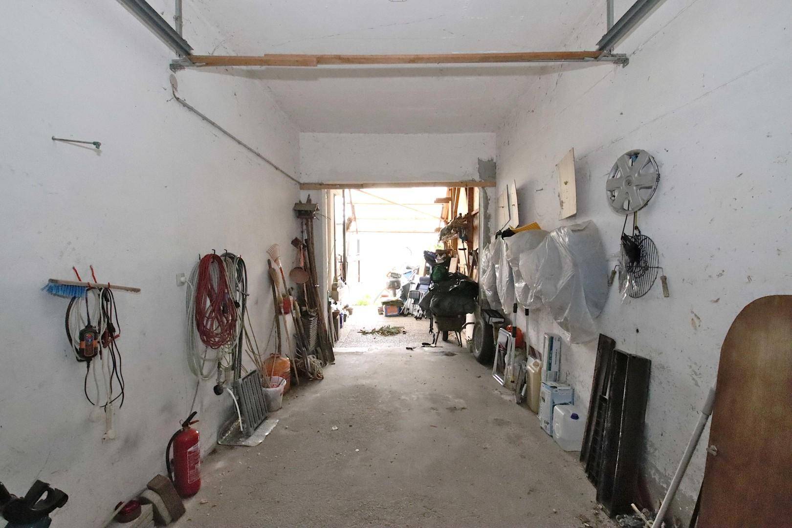 Lange Garage mit offenem Tor, Blick ins Freie und vielseitigem Stauraum an den Wänden.