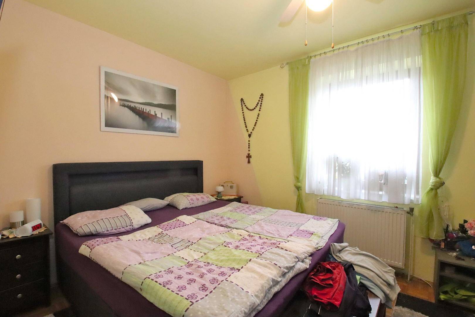 Schlafzimmer mit Doppelbett, hellgrünen Vorhängen, gelben Wänden und Deckenventilator.