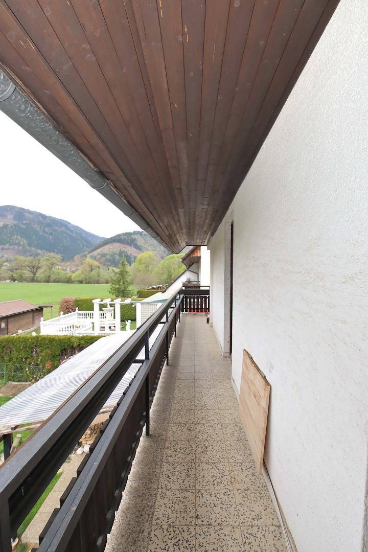 Langer Balkon mit Fliesenboden, Holzdecke und einem weiten Blick auf die Berge.