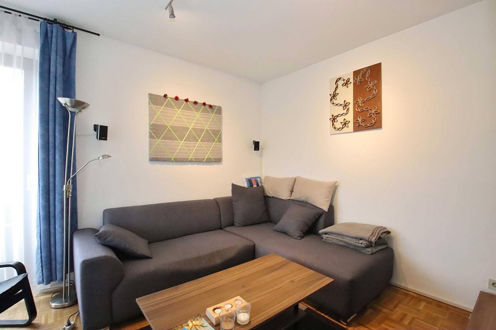 Modernes Wohnzimmer mit grauem Ecksofa, Holztisch und blauen Vorhängen.