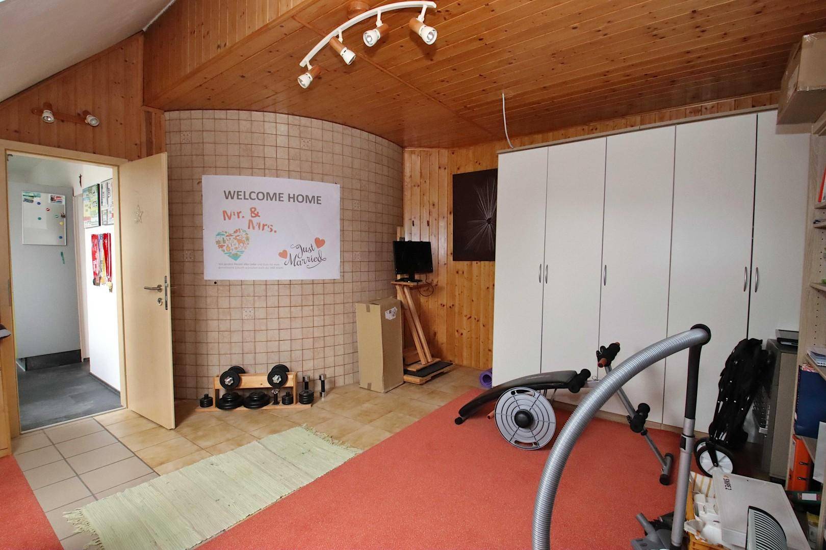 Vielseitiger Raum mit Holzverkleidung, genutzt als Fitnessbereich und Stauraum.