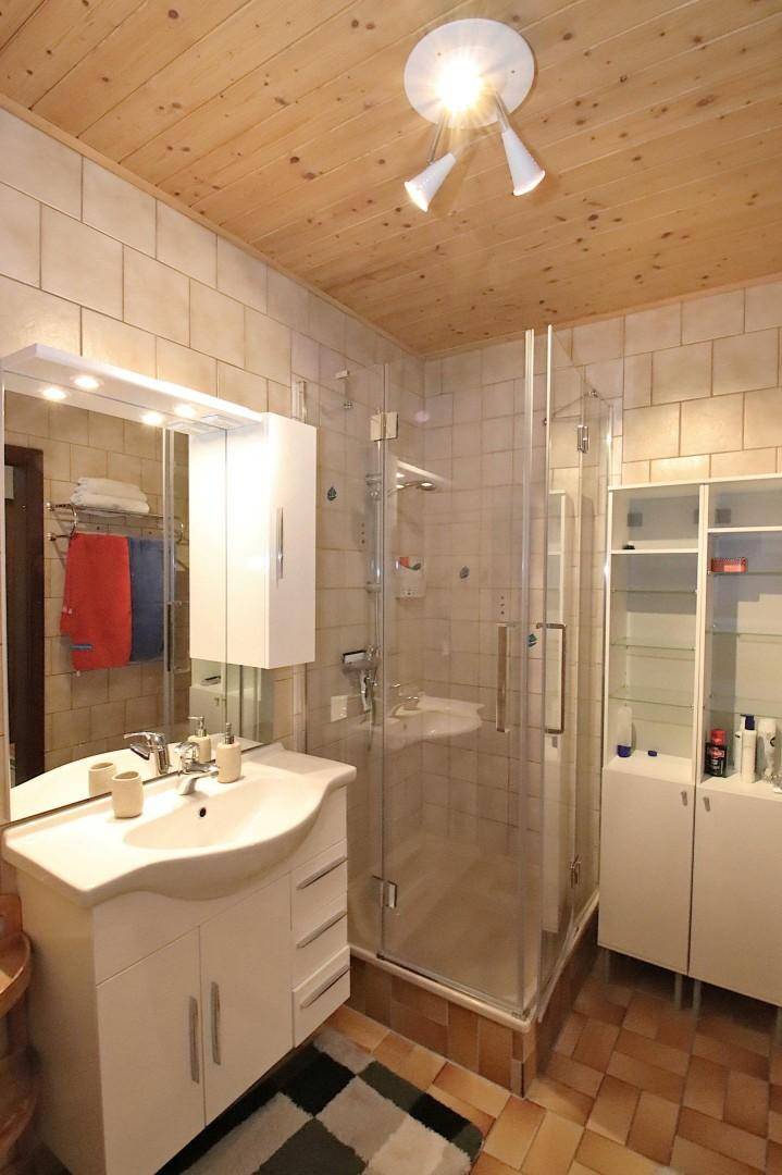 Badezimmer mit Holzdecke, gefliesten Wänden, Glasduschkabine und modernem Waschtisch.