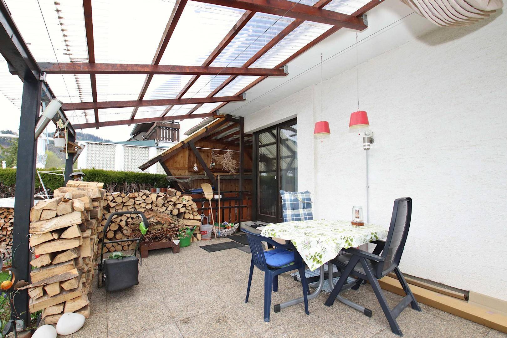 Überdachte Terrasse mit Gartenmöbeln und einem großen Holzstapel für gemütliche Abende.