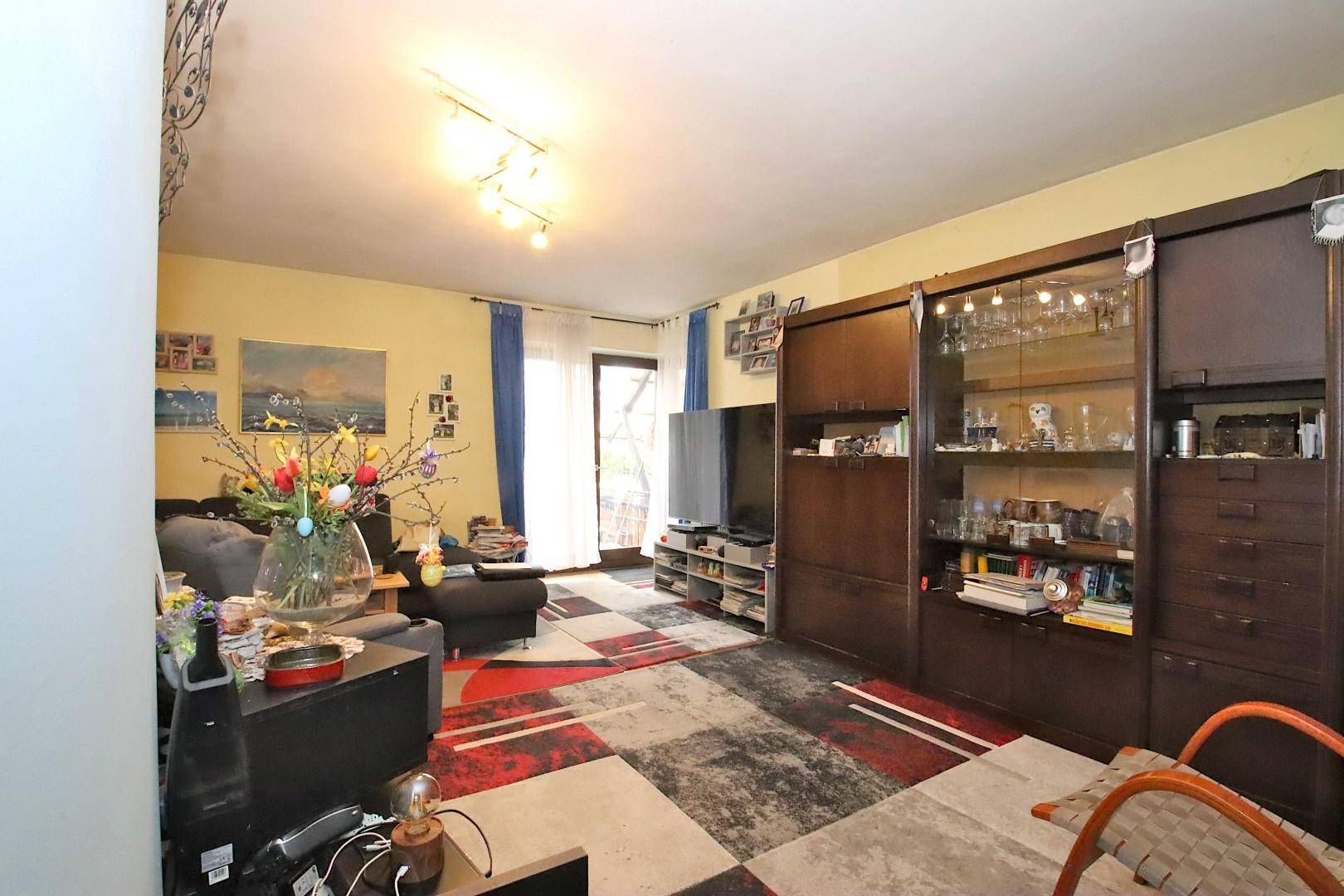 Gemütliches Wohnzimmer mit dunklen Möbeln, farbenfrohem Teppich und Zugang zum Balkon.